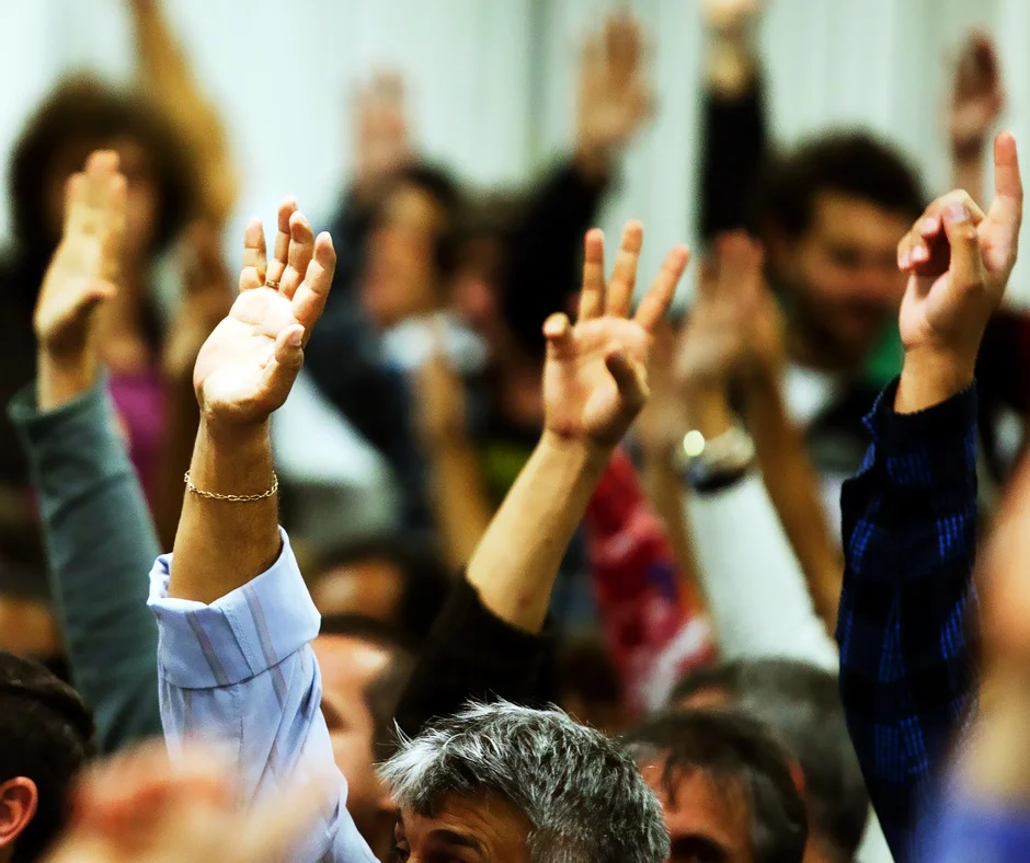 Pessoas com as mãos levantadas em assembleia popular